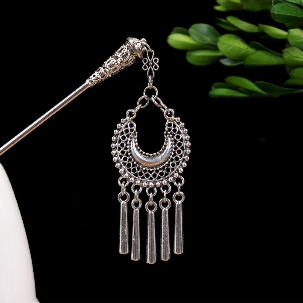 Boho vintage ethnic silver-tone hair stick featuring turquoise beads, an intricate round decorative element, and layered chain tassel fringe, displayed beside a white vessel green foliage 01