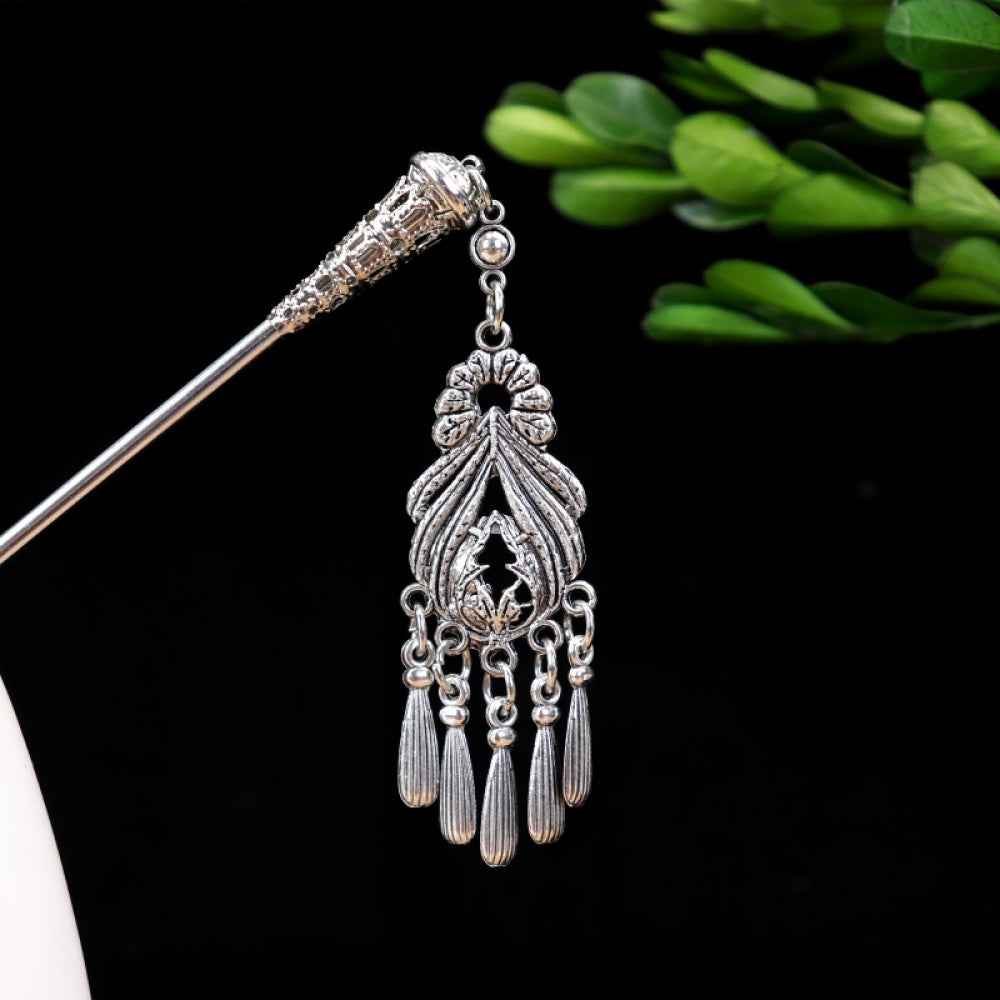 Boho vintage ethnic silver-tone hair stick featuring turquoise beads, an intricate round decorative element, and layered chain tassel fringe, displayed beside a white vessel green foliage 04