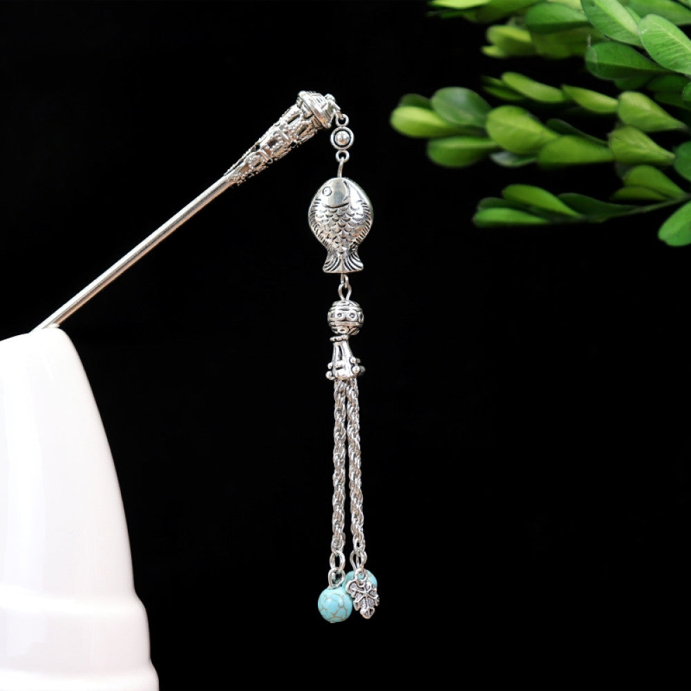 Boho vintage ethnic silver-tone hair stick featuring turquoise beads, an intricate round decorative element, and layered chain tassel fringe, displayed beside a white vessel green foliage 06