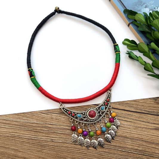 Boho vintage ethnic tri-color (black/red/green) rope choker necklace, featuring a silver-tone ornate fringe pendant with colorful bead details, displayed on a wooden surface (paired with white background, green foliage & a notebook), ideal for bohemian casual fashion styling in the US 01
