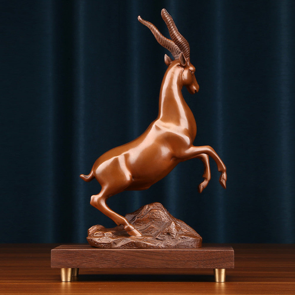 Bronze antelope statue with a leaping stance, a Feng Shui symbol of success and strength, displayed on a wooden base as elegant home decor against a dark blue background