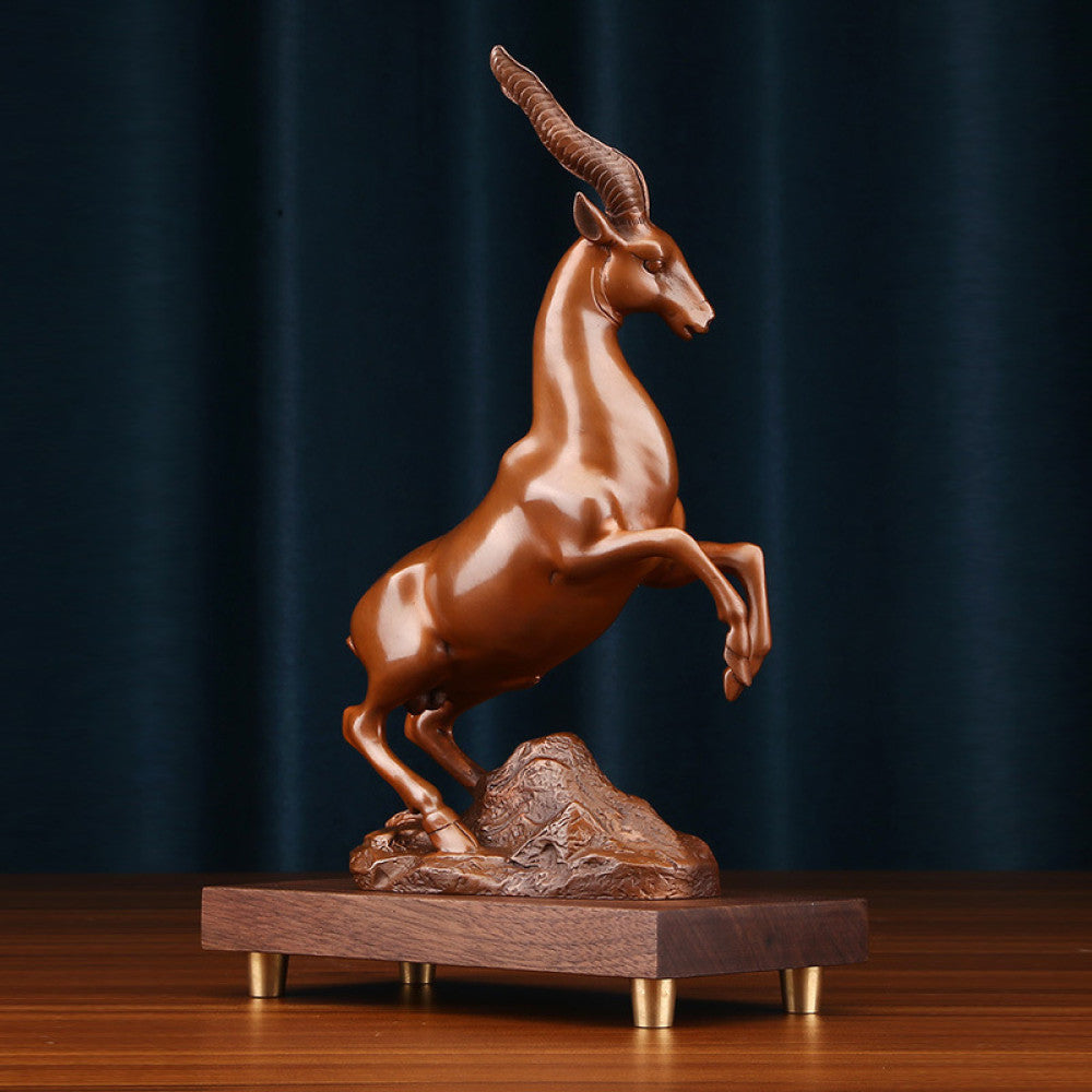 Bronze antelope statue with a leaping stance, a Feng Shui symbol of success and strength, displayed on a wooden base as elegant home decor against a dark blue background
