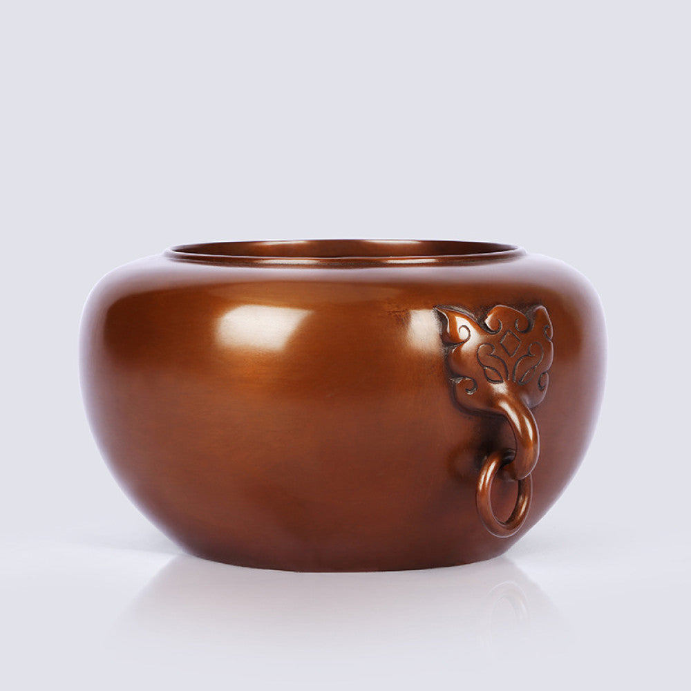 Polished bronze Chinese censer with intricate beast-head handle and ring, a Feng Shui symbol of wealth and harmony, displayed as elegant home decor against a light background