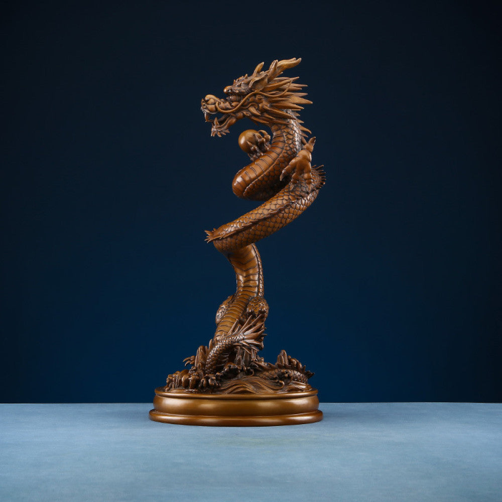 Intricate bronze Chinese dragon statue coiled around a pearl, a symbol of power and good fortune in Feng Shui, displayed on a blue surface against a dark blue background