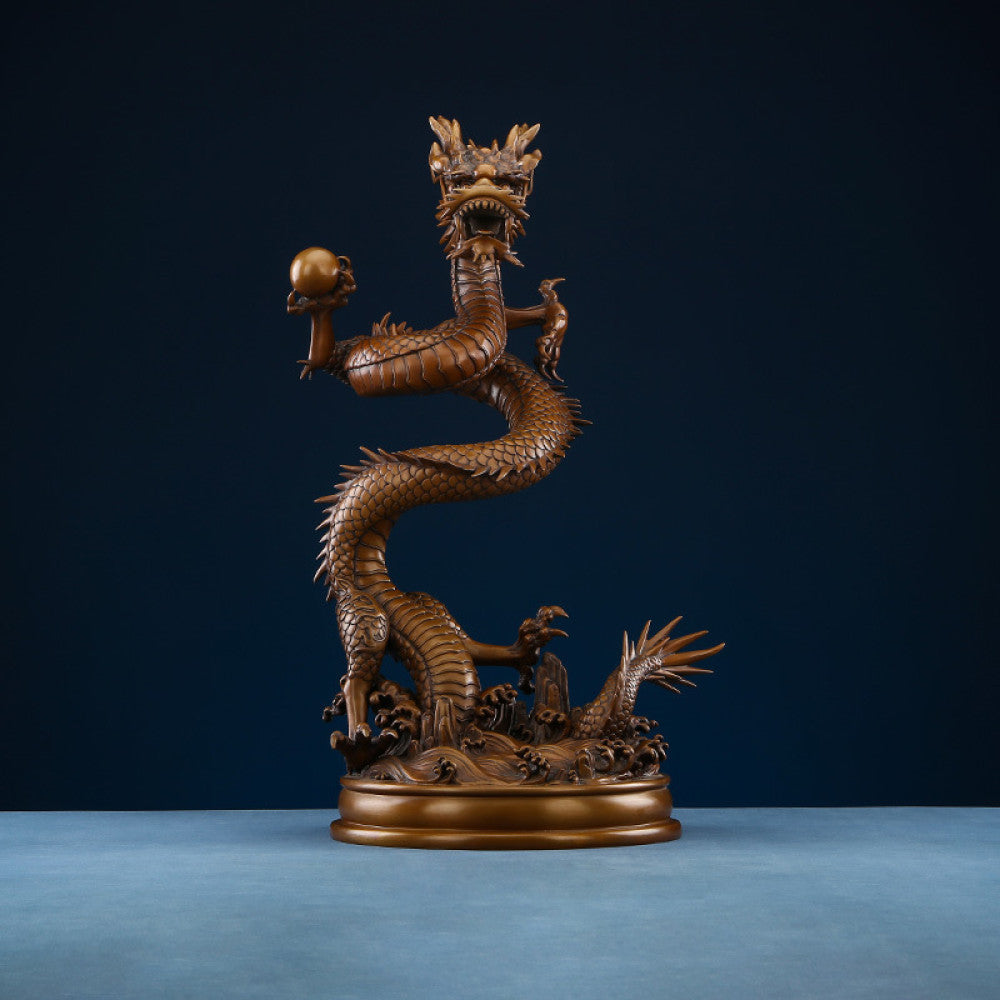 Intricate bronze Chinese dragon statue coiled around a pearl, a symbol of power and good fortune in Feng Shui, displayed on a blue surface against a dark blue background 01