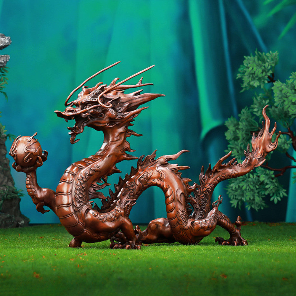 Intricate bronze Chinese dragon statue holding a pearl, a Feng Shui symbol of good fortune and strength, displayed as elegant home decor in a natural-inspired setting against a green background