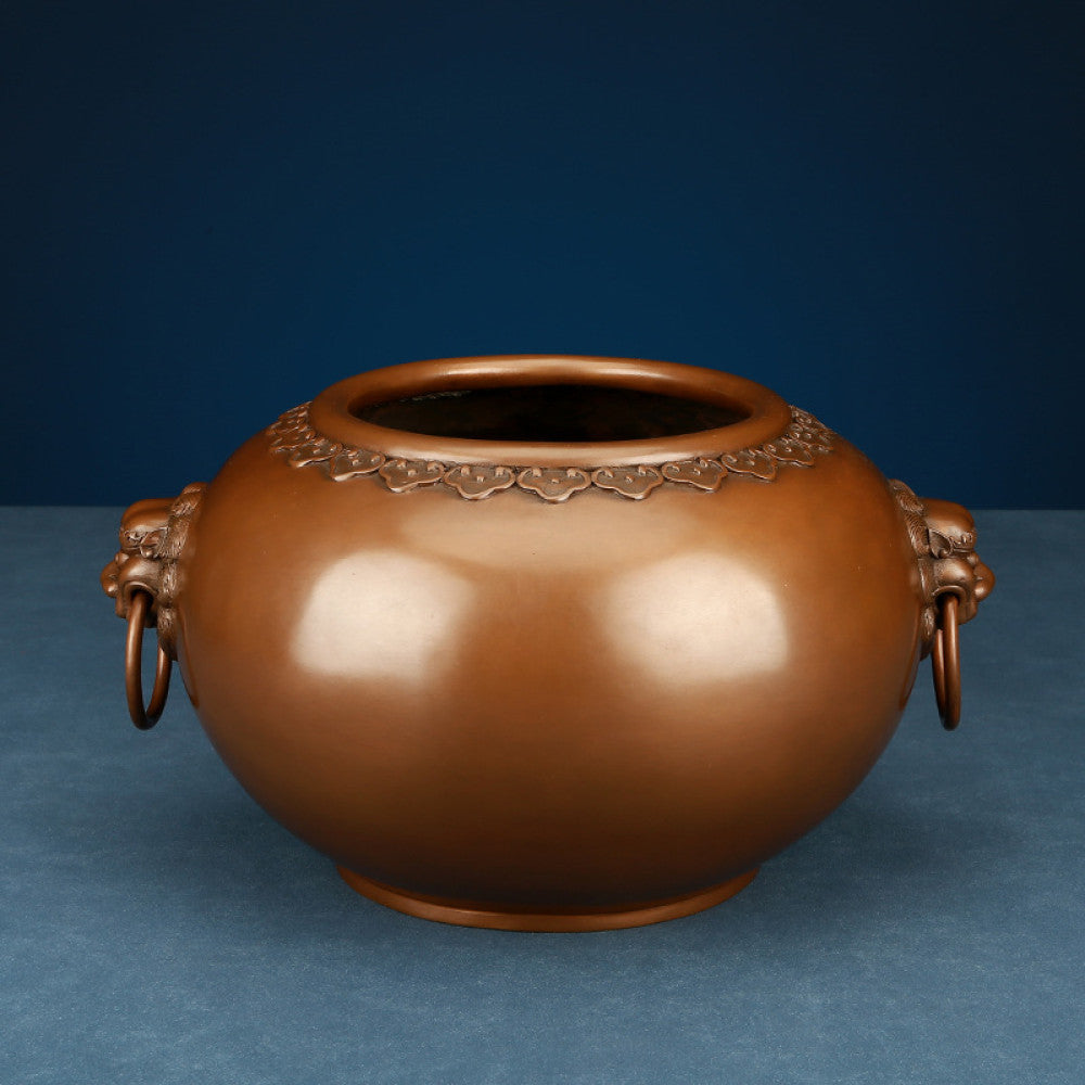 Polished bronze Chinese incense burner with intricate beast-head handles and decorative rim, a Feng Shui symbol of wealth and protection, displayed as elegant home decor against a dark blue background on a textured surface