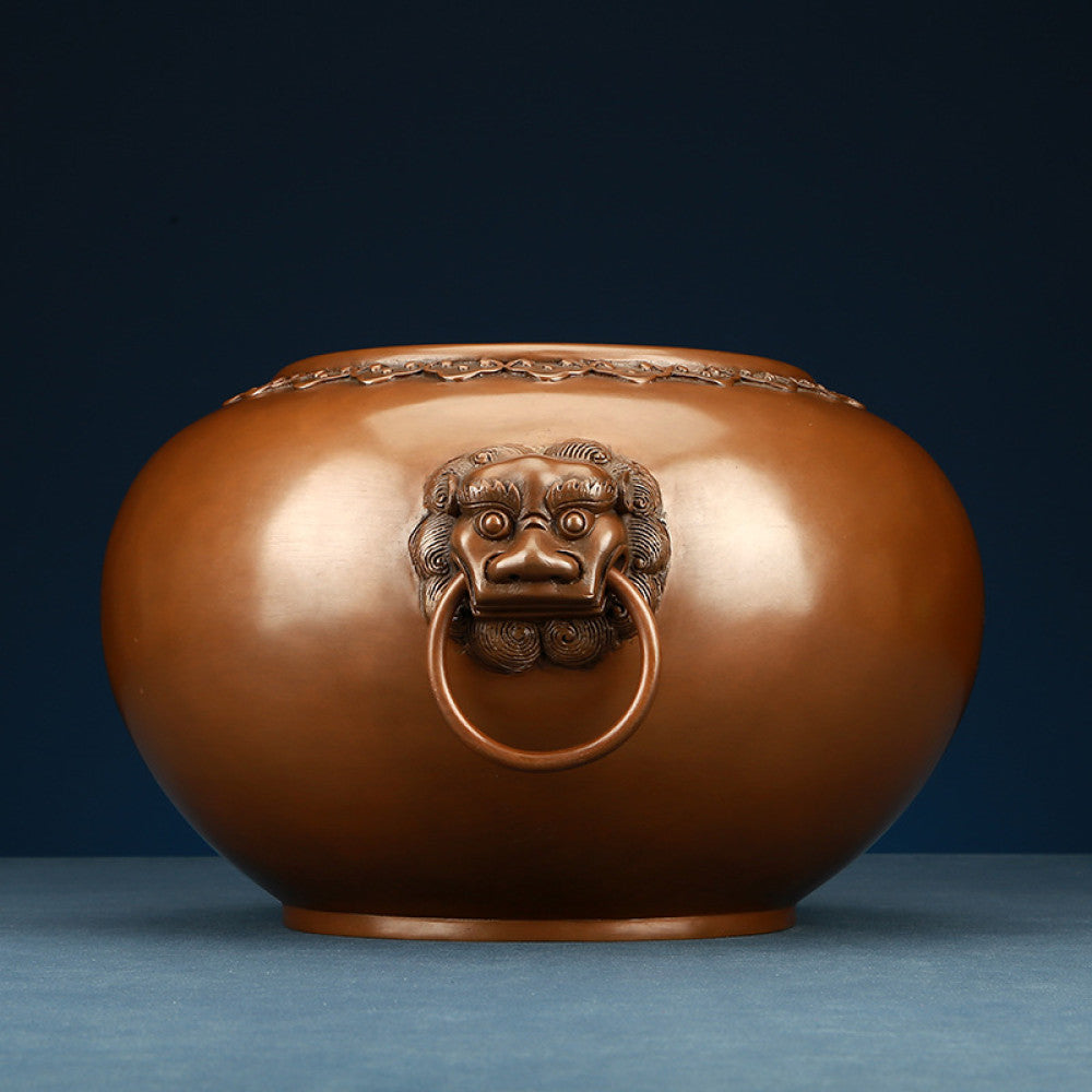 Polished bronze Chinese incense burner with intricate beast-head handles and decorative rim, a Feng Shui symbol of wealth and protection, displayed as elegant home decor against a dark blue background on a textured surface 01