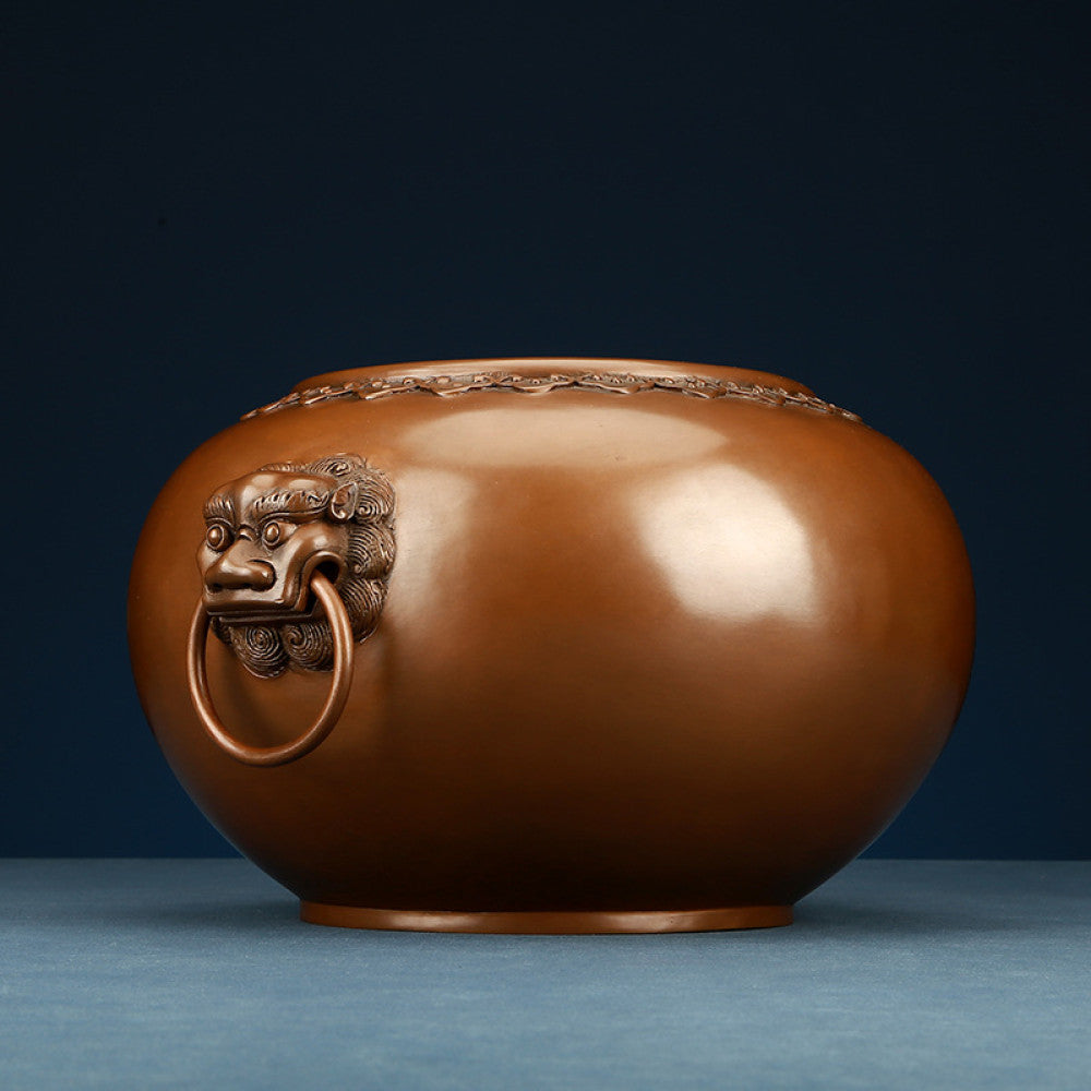 Polished bronze Chinese incense burner with intricate beast-head handles and decorative rim, a Feng Shui symbol of wealth and protection, displayed as elegant home decor against a dark blue background on a textured surface 04