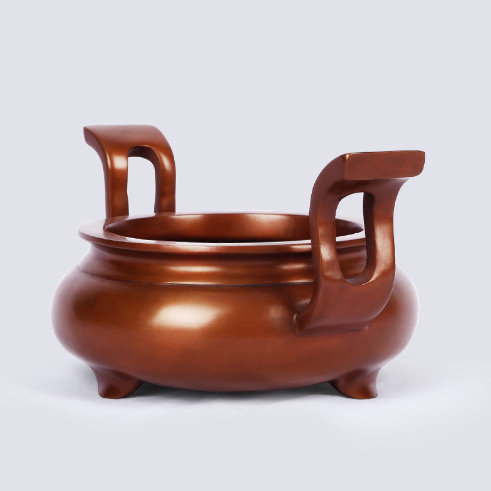 Polished bronze Chinese incense burner with elegant curved handles and three feet, a Feng Shui symbol of wealth and harmony, displayed as refined home decor against a white background