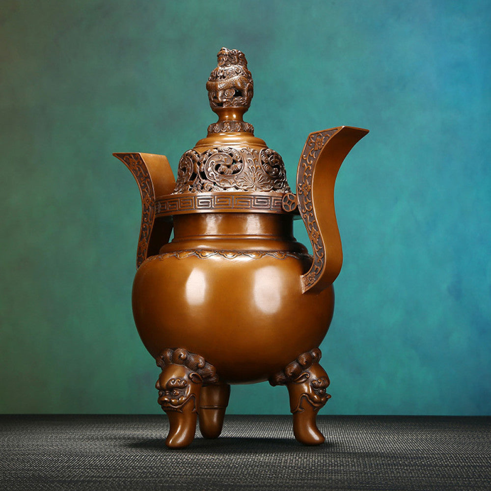 Intricate bronze Chinese incense burner with dragon-topped pierced lid, ornate curved handles, and lion-shaped feet, a Feng Shui symbol of wealth and elegance, displayed as a sophisticated home decor piece against a teal textured background 03