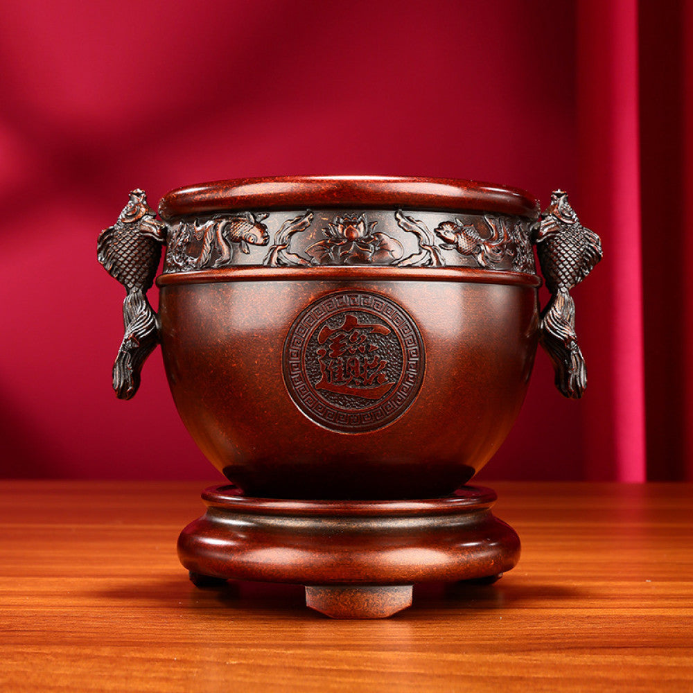 Intricate bronze Chinese incense burner with fish-shaped handles, “Wealth & Prosperity” carvings, and a decorative base, a Feng Shui symbol of good fortune, displayed as elegant home decor on a wooden surface against a red background