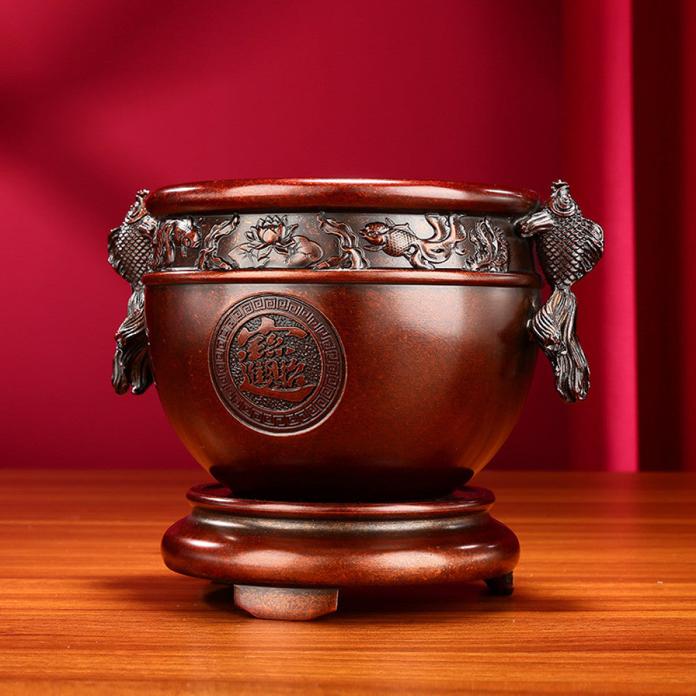 Intricate bronze Chinese incense burner with fish-shaped handles, “Wealth & Prosperity” carvings, and a decorative base, a Feng Shui symbol of good fortune, displayed as elegant home decor on a wooden surface against a red background 01