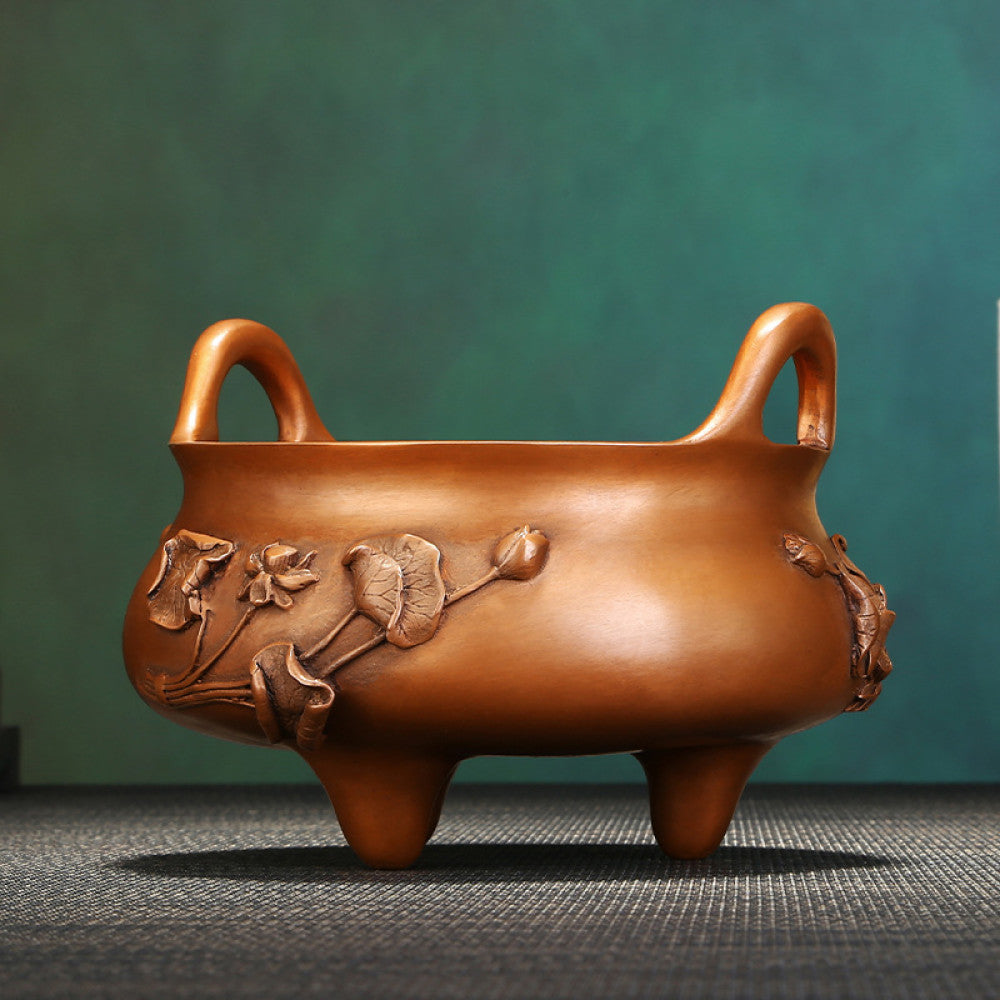 Intricate bronze Chinese incense burner with raised lotus flower carvings, curved handles, and three feet, a Feng Shui symbol of wealth and harmony, displayed as elegant home decor on a textured surface against a teal background 01