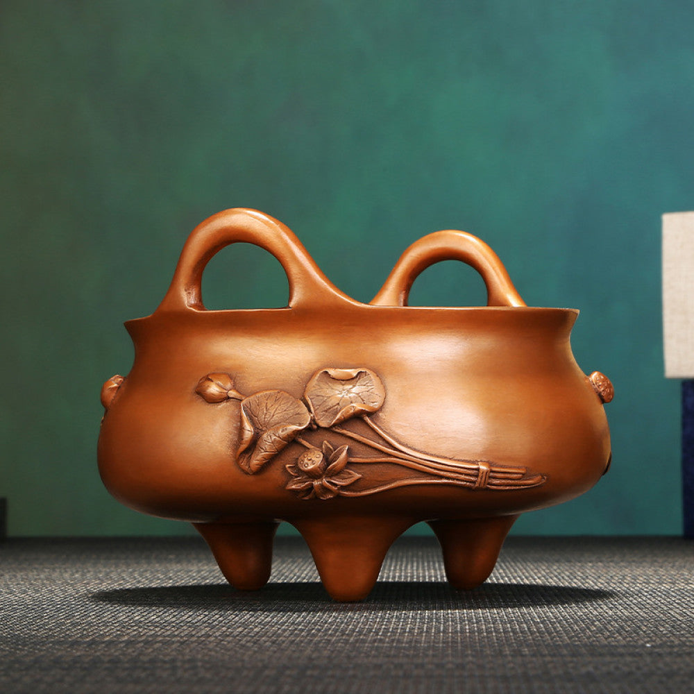 Intricate bronze Chinese incense burner with raised lotus flower carvings, curved handles, and three feet, a Feng Shui symbol of wealth and harmony, displayed as elegant home decor on a textured surface against a teal background 02