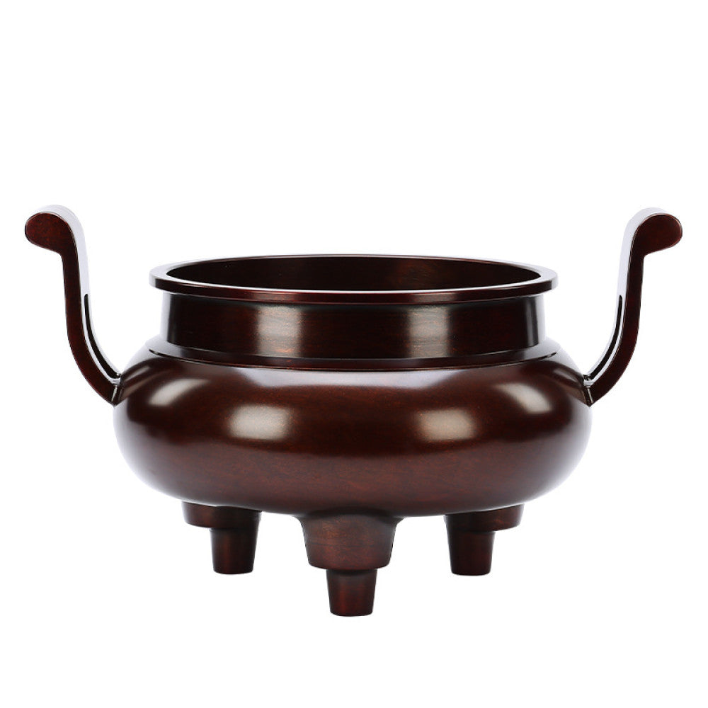 Intricate bronze Chinese incense burner with traditional curved handles and three feet, a Feng Shui symbol of wealth and harmony, displayed as elegant home decor on a wooden surface against a red background 02