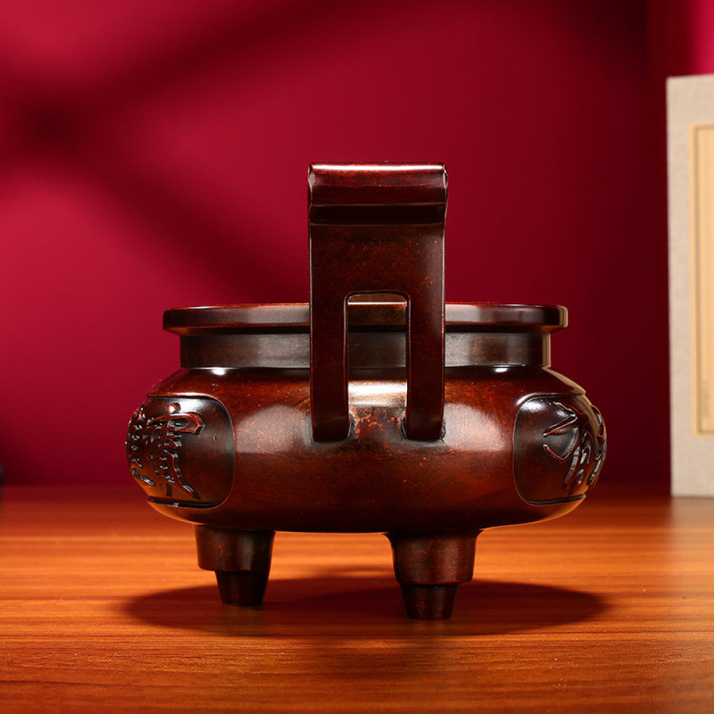 Intricate bronze Chinese incense burner with traditional curved handles, three feet, and "Wealth & Prosperity" carvings, a Feng Shui symbol of good fortune, displayed as elegant home decor on a wooden surface against a red background 01