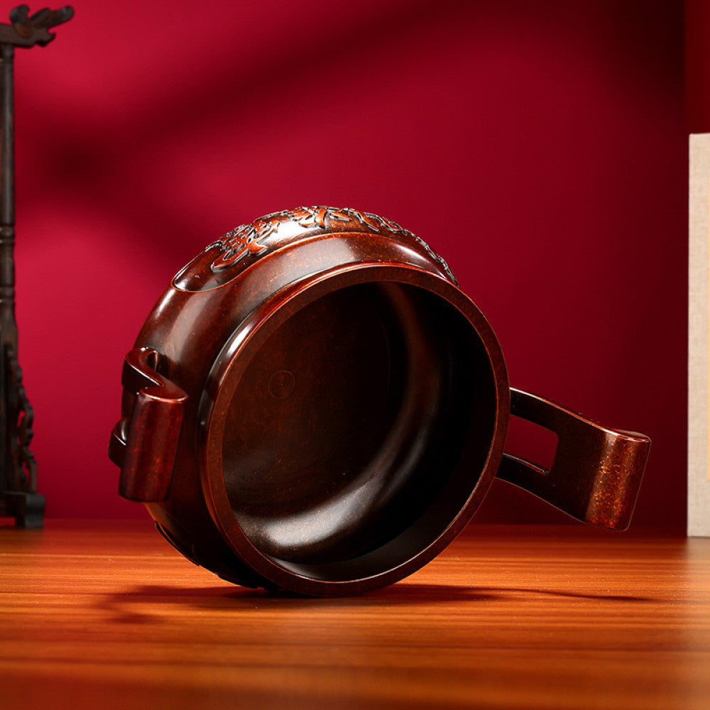Intricate bronze Chinese incense burner with traditional curved handles, three feet, and "Wealth & Prosperity" carvings, a Feng Shui symbol of good fortune, displayed as elegant home decor on a wooden surface against a red background 02