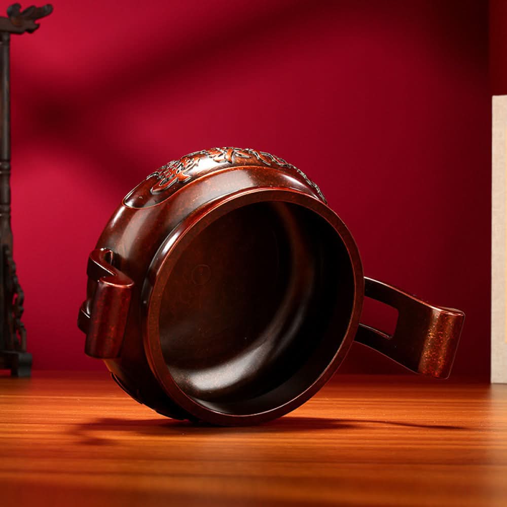 Intricate bronze Chinese incense burner with traditional curved handles, three feet, and "Wealth & Prosperity" carvings, a Feng Shui symbol of good fortune, displayed as elegant home decor on a wooden surface against a red background 02