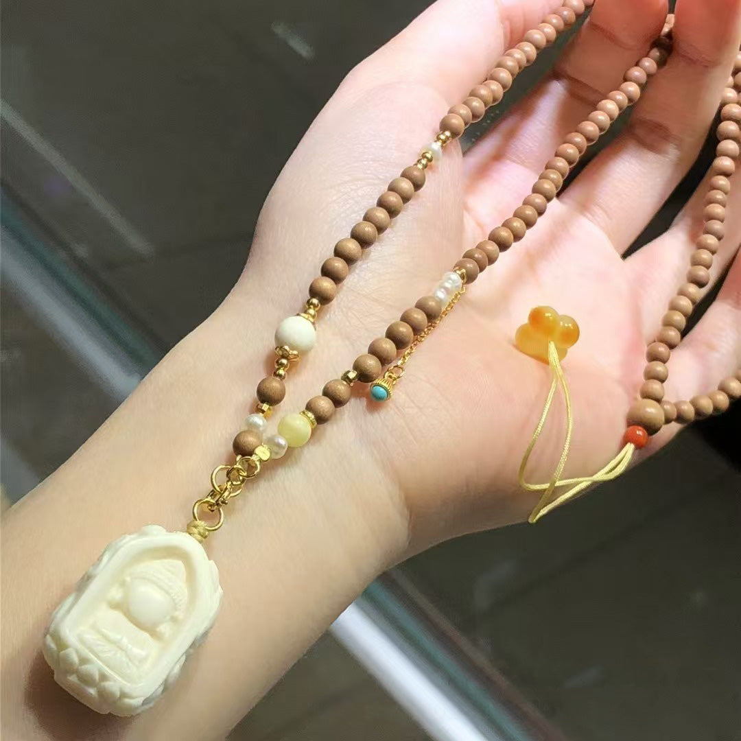 A necklace with a carved Buddha ivory nut pendant, wooden beads, and accents of white jade bodhi, amber, turquoise, and red agate, held in a hand