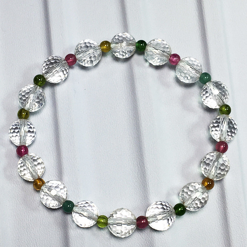 A beaded bracelet featuring clear, textured crystal beads interspersed with small multi - colored gemstone beads in shades of green, red, and yellow, arranged in a circular design and displayed on a light - colored fabric background.