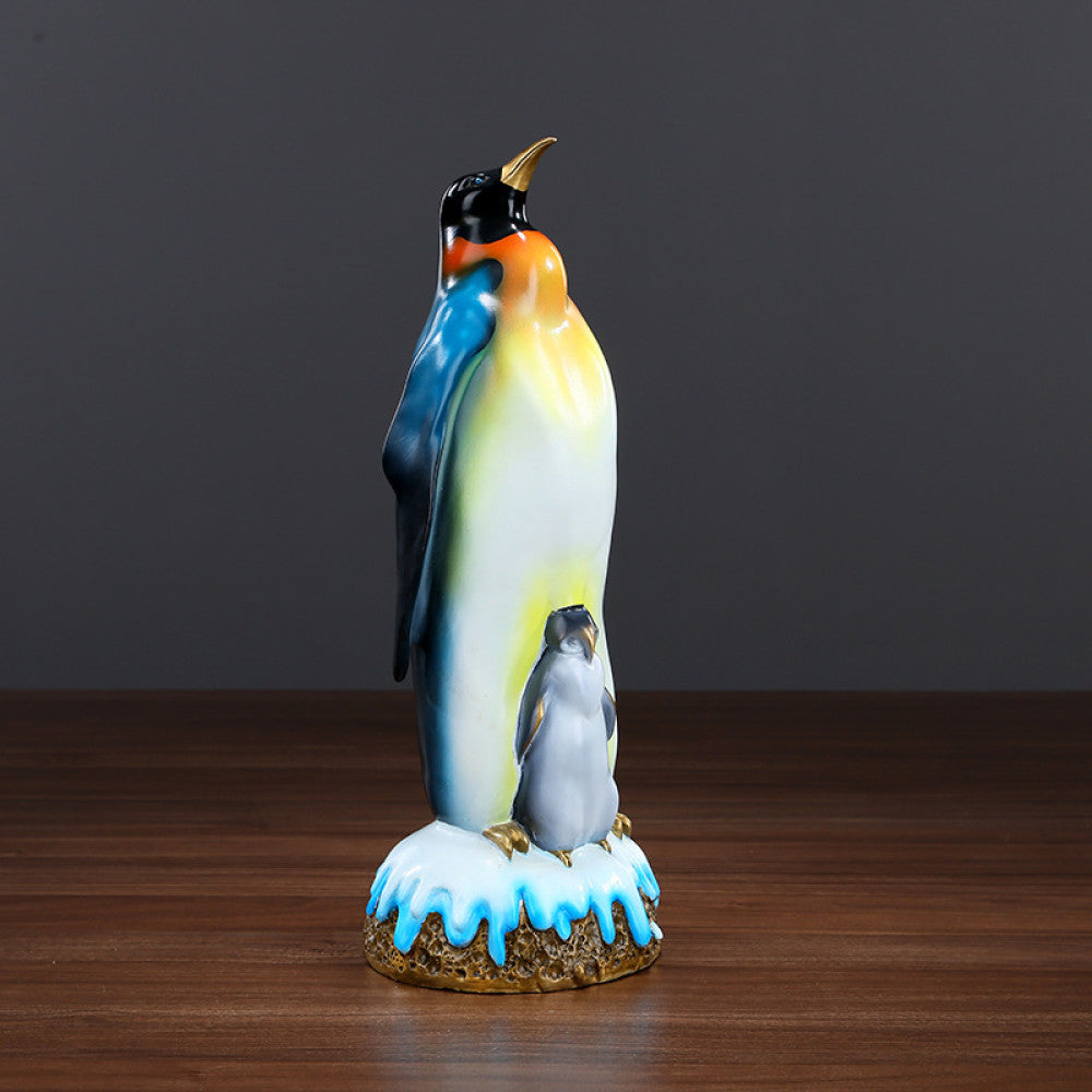 Colorful penguin statue featuring an adult penguin and a chick, designed as a charming home decor accent piece with a snow - themed base, displayed on a wooden surface against a gray background