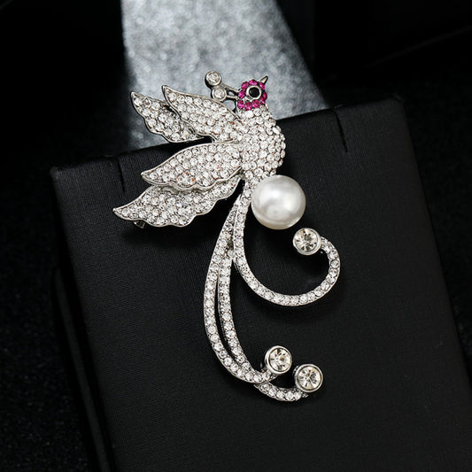 This elegant brooch features a sparkling crystal-encrusted bird in a gold-tone setting, accented by a lustrous pearl and delicate pink detail at its head. A sophisticated statement piece for any outfit 01