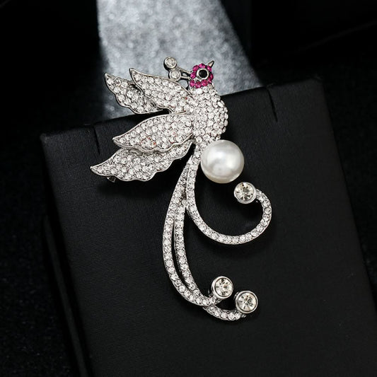 This elegant brooch features a sparkling crystal-encrusted bird in a gold-tone setting, accented by a lustrous pearl and delicate pink detail at its head. A sophisticated statement piece for any outfit 01