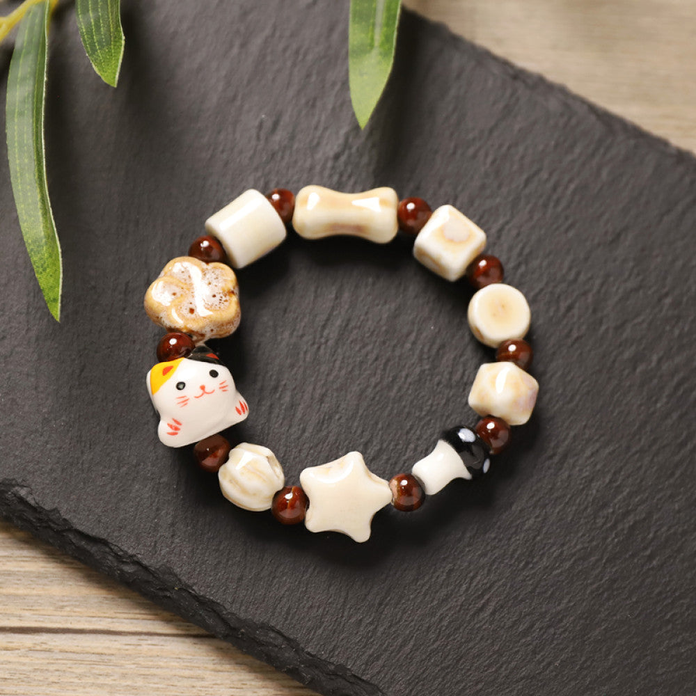 This playful beaded bracelet features a charming lucky cat ceramic bead at its center, paired with whimsical ceramic charms like stars, bones, and flowers, interspersed with small brown beads. Crafted from ceramic, it brings a cute, kawaii vibe to everyday outfits
