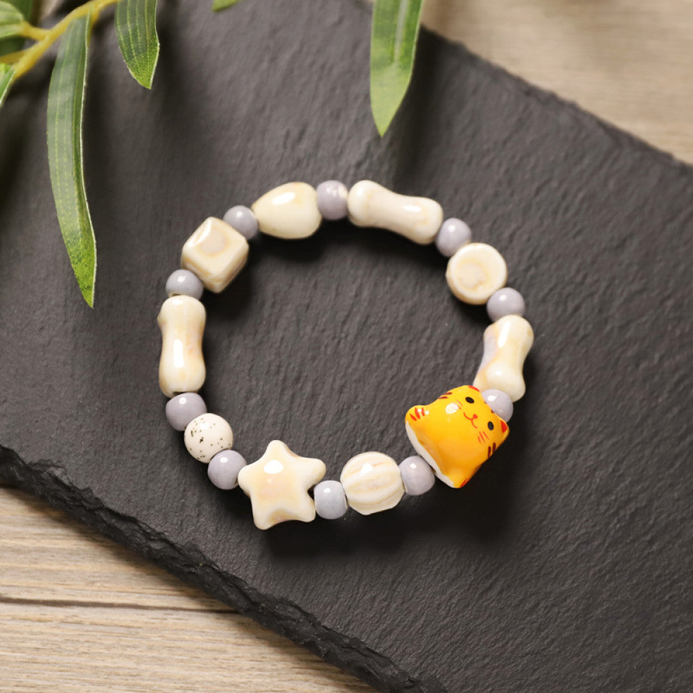 This playful beaded bracelet features a charming lucky cat ceramic bead at its center, paired with whimsical ceramic charms like stars, bones, and flowers, interspersed with small brown beads. Crafted from ceramic, it brings a cute, kawaii vibe to everyday outfits 03