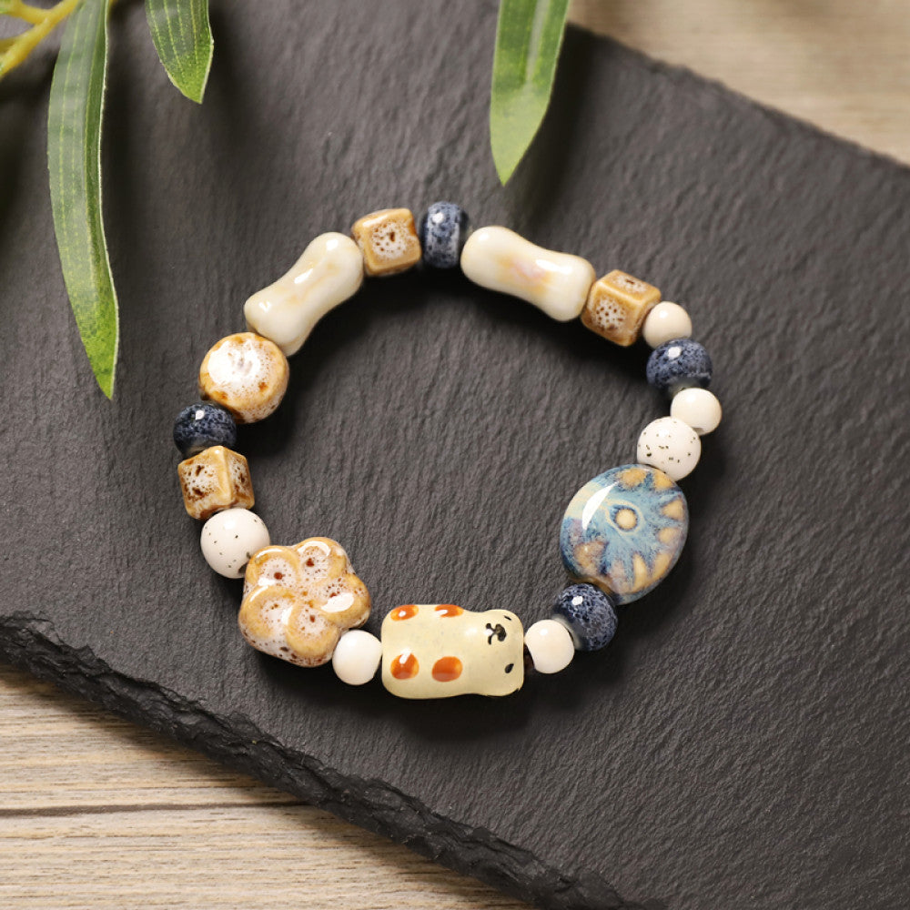 This playful beaded bracelet features a charming lucky cat ceramic bead at its center, paired with whimsical ceramic charms like stars, bones, and flowers, interspersed with small brown beads. Crafted from ceramic, it brings a cute, kawaii vibe to everyday outfits 05