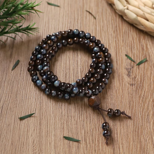 Deep brown patterned beads, textured and antique, with small tassel pendant.