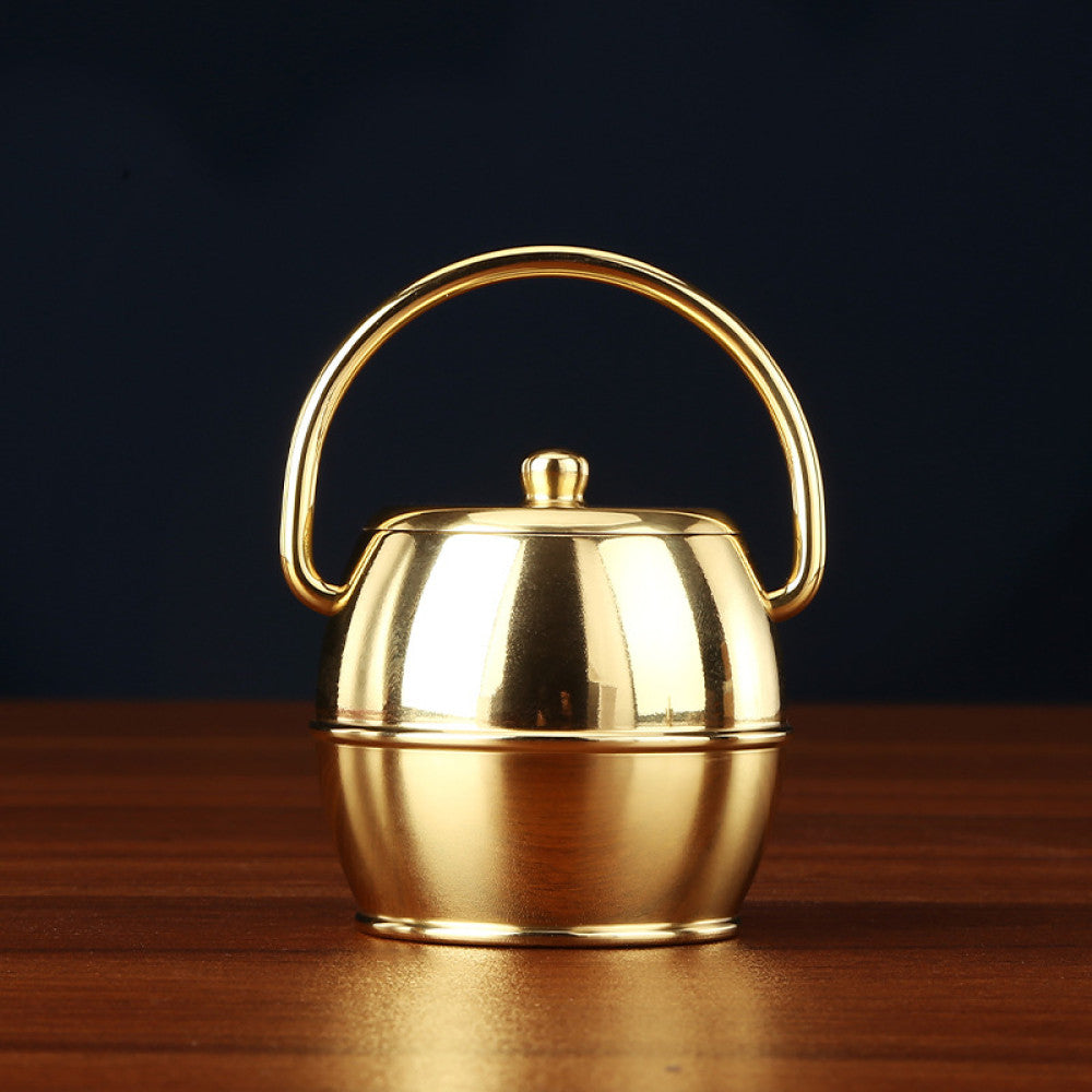 Golden brass handled teapot with lid placed on wooden table against dark background