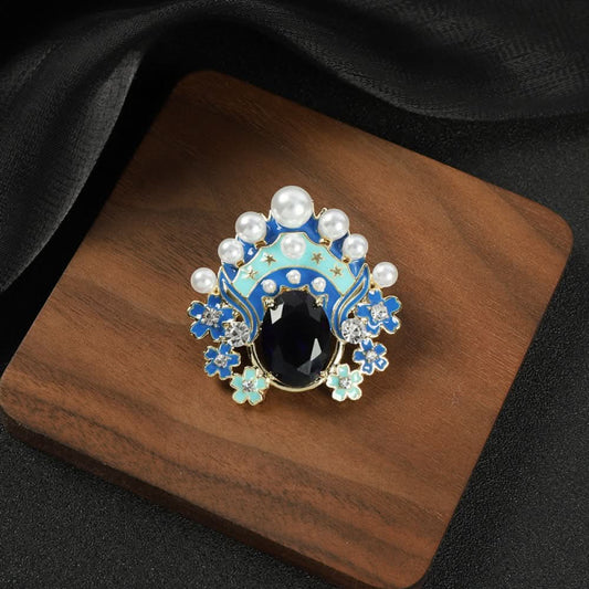 This striking brooch features a bold, theatrical-inspired design with vibrant enamel, lustrous pearls, and a prominent red crystal at its center. Delicate floral motifs and sparkling crystals add intricate detail, making it a standout accessory for blazers, scarves, or dresses. Perfect for adding a pop of color and artistic flair to any outfit, this piece is sure to make a memorable statement. 01