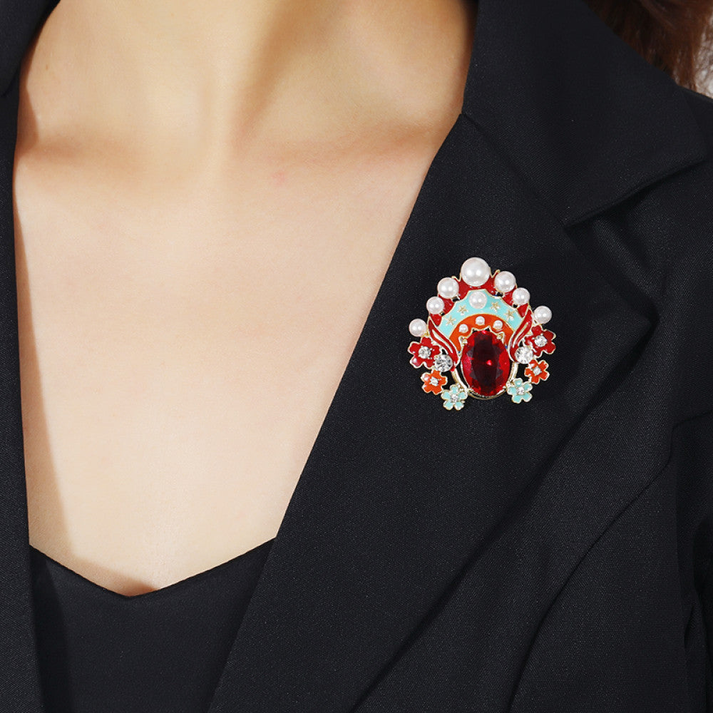 This striking brooch features a bold, theatrical-inspired design with vibrant enamel, lustrous pearls, and a prominent red crystal at its center. Delicate floral motifs and sparkling crystals add intricate detail, making it a standout accessory for blazers, scarves, or dresses. Perfect for adding a pop of color and artistic flair to any outfit, this piece is sure to make a memorable statement. 02