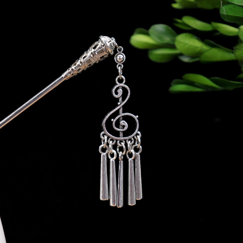 silver-tone hair stick featuring turquoise beads, an intricate round decorative element, and layered chain tassel fringe, displayed beside a white vessel green foliage 02