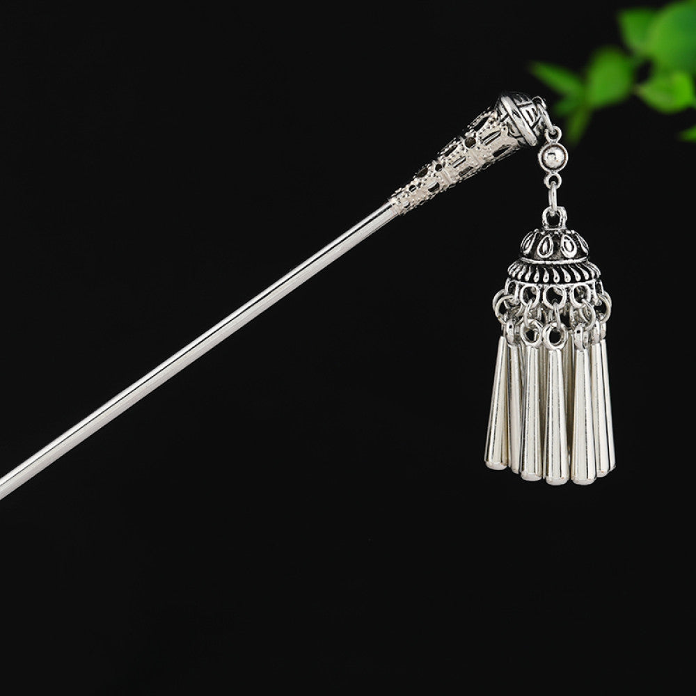 silver-tone hair stick featuring turquoise beads, an intricate round decorative element, and layered chain tassel fringe, displayed beside a white vessel green foliage 05
