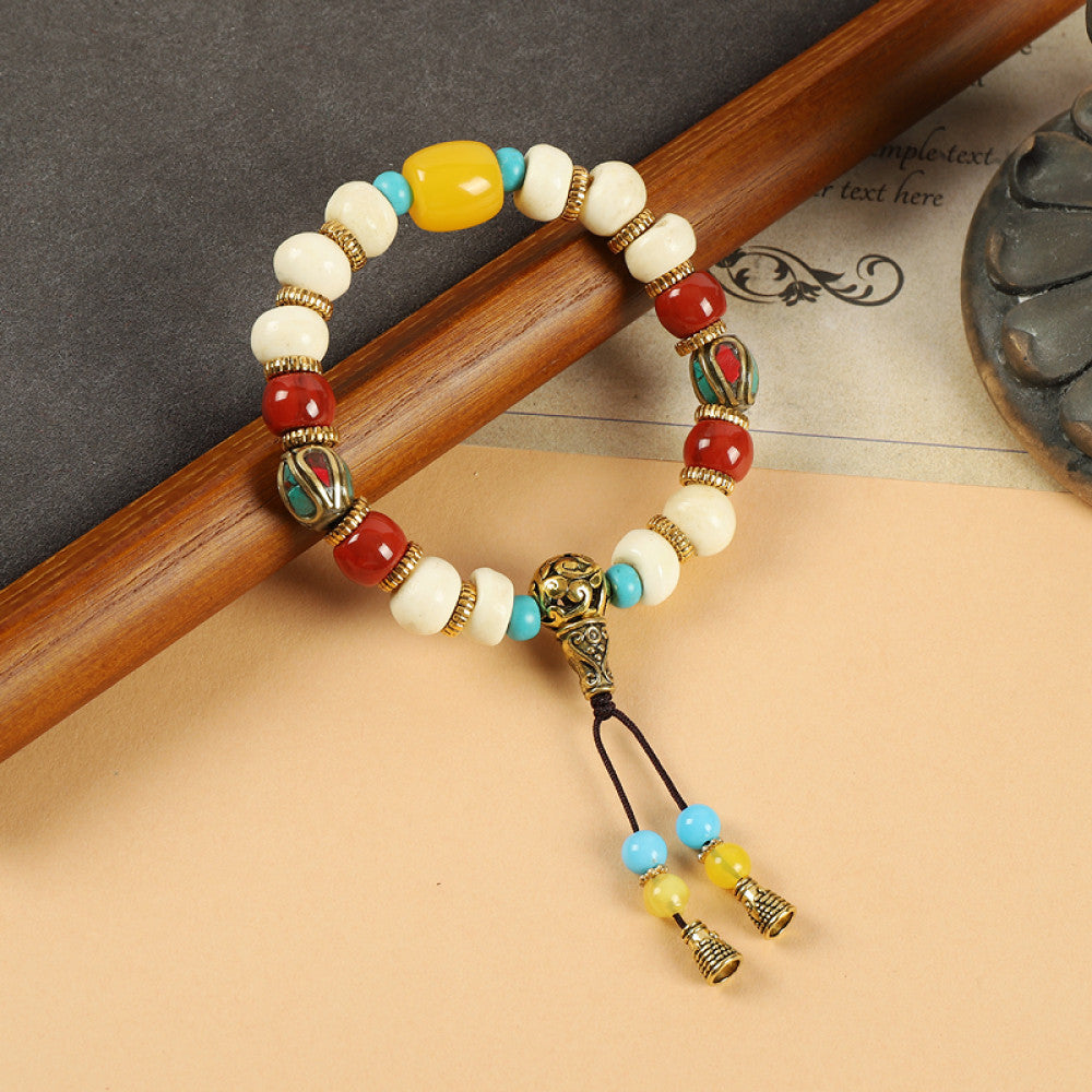 This ethnic-style bracelet features a mix of white, yellow, and red ceramic beads, accented with turquoise details and an adjustable tassel closure for a unique, cultural-inspired loo