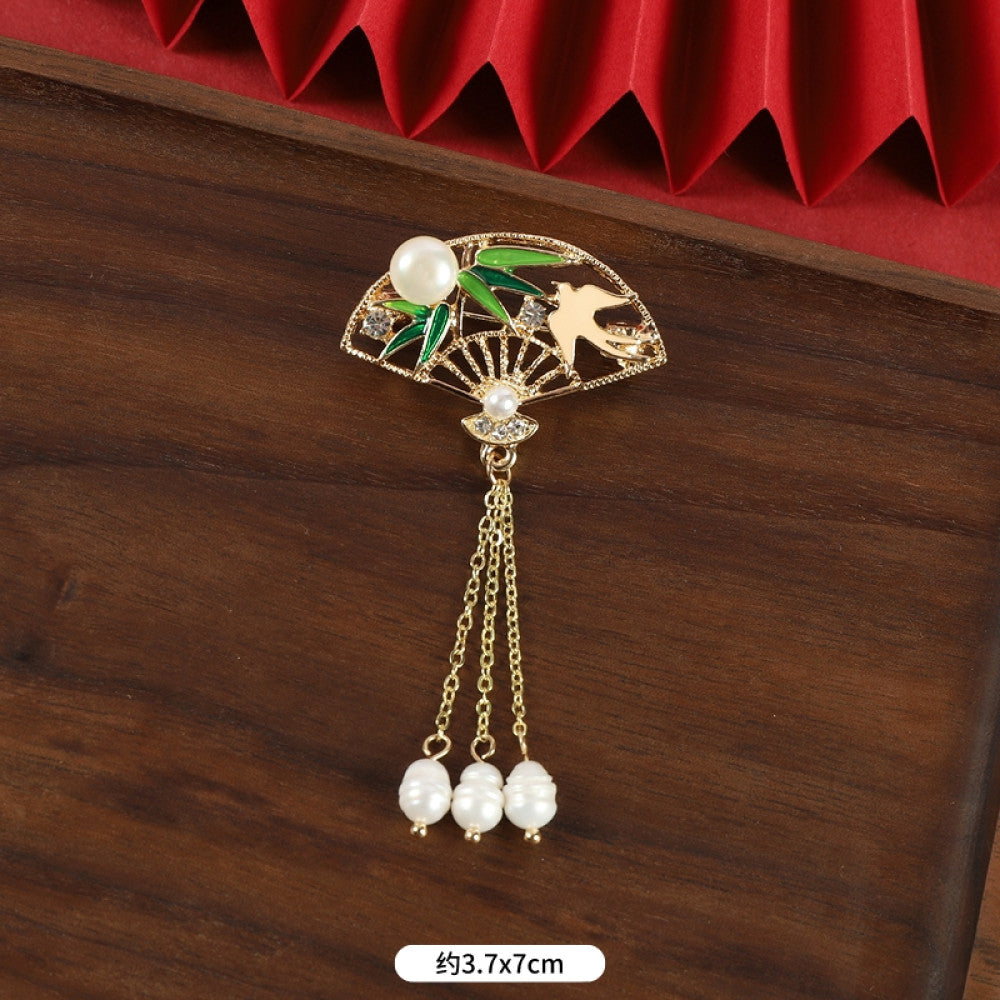 This elegant brooch features a delicate fan-shaped design, crafted with a gold-tone metal frame and adorned with vibrant multicolored gemstones. A lustrous pearl anchors the center, from which three graceful gold chains dangle, each finished with a small pearl drop. Perfect for adding a touch of sophistication to blazers, scarves, or special occasion outfits, this piece blends intricate craftsmanship with timeless, eye-catching charm 06