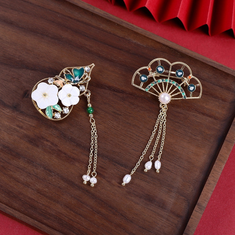 This elegant brooch features a delicate fan-shaped design, crafted with a gold-tone metal frame and adorned with vibrant multicolored gemstones. A lustrous pearl anchors the center, from which three graceful gold chains dangle, each finished with a small pearl drop. Perfect for adding a touch of sophistication to blazers, scarves, or special occasion outfits, this piece blends intricate craftsmanship with timeless, eye-catching charm 07