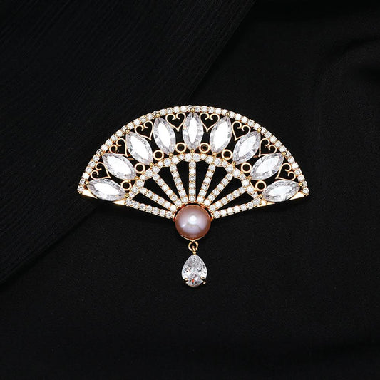 This elegant brooch features a striking fan-shaped design, crafted with a gold-tone metal base. It is adorned with vibrant emerald-green gemstones, shimmering clear crystals, and a lustrous pearl at the center, from which a teardrop-shaped green gem dangles gracefully. Perfect for adding a touch of sophistication to blazers, scarves, or evening wear, this piece blends timeless elegance with a bold, eye-catching silhouette.01