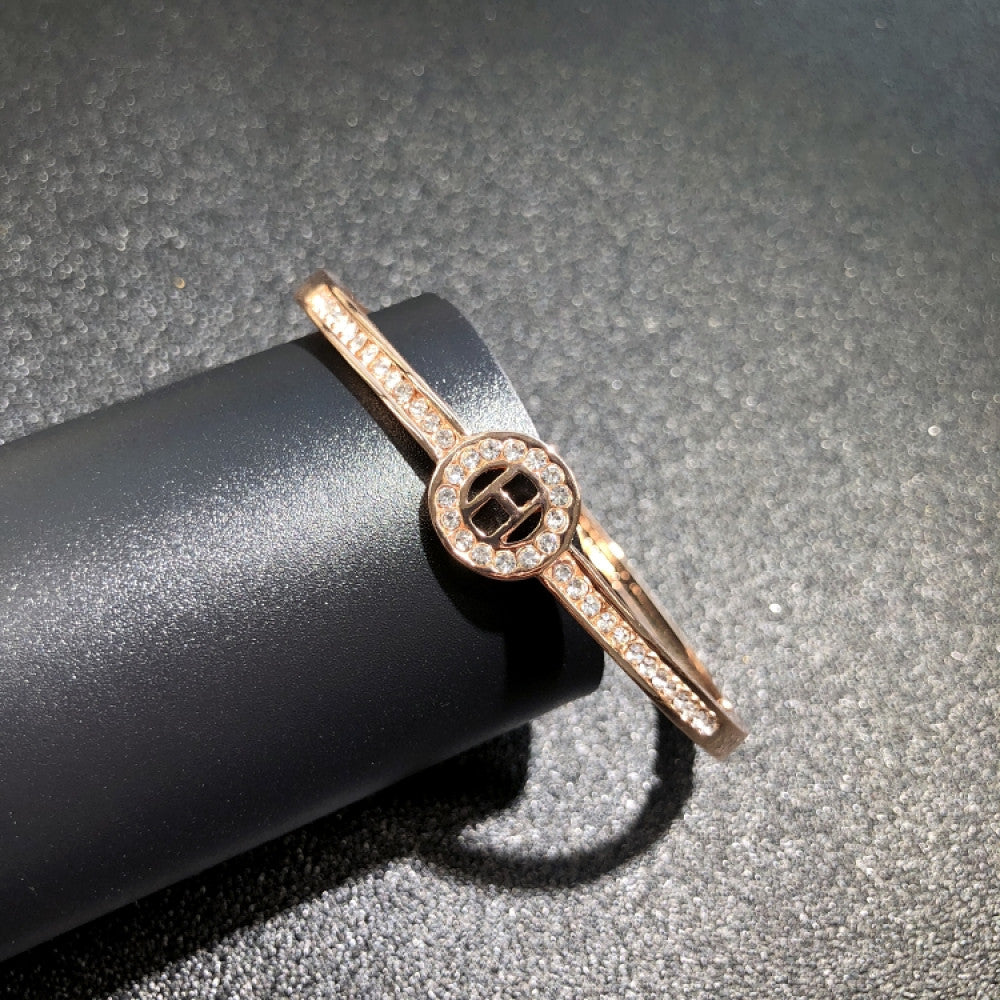 Fashion luxury rose gold bangle with diamond-encrusted signature logo, displayed on black surface, ideal for luxury fashion and statement jewelry enthusiasts