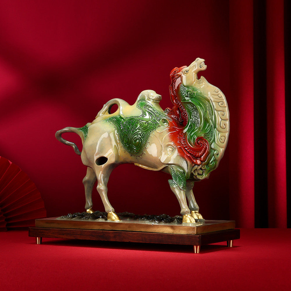 Colorful camel statue with intricate details, symbolizing good fortune in feng shui, placed on a wooden base against a vibrant red background with traditional Chinese fan decor