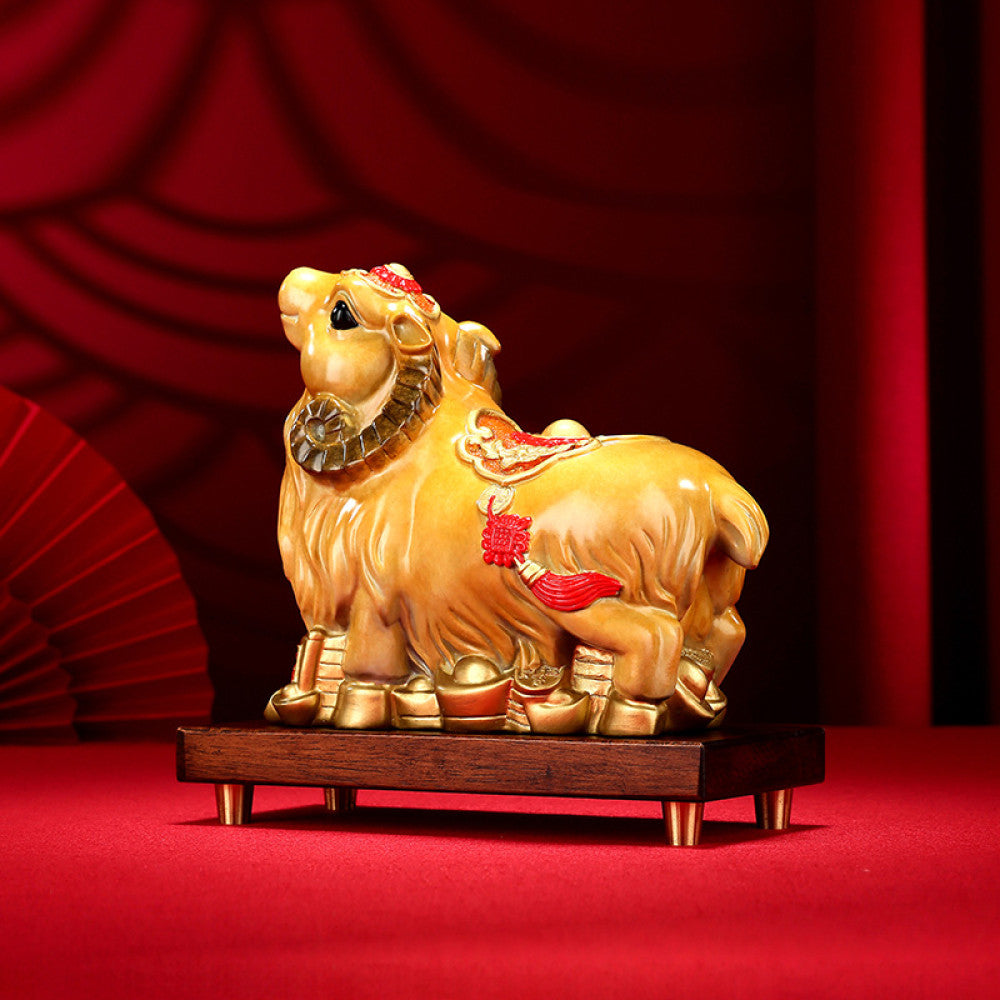 Golden camel statue with red accents and lucky details, a Feng Shui symbol of good fortune, displayed on a wooden base against a red background with a traditional fan decor