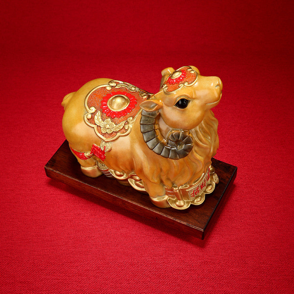 Golden camel statue with red accents and lucky details, a Feng Shui symbol of good fortune, displayed on a wooden base against a red background with a traditional fan decor 01