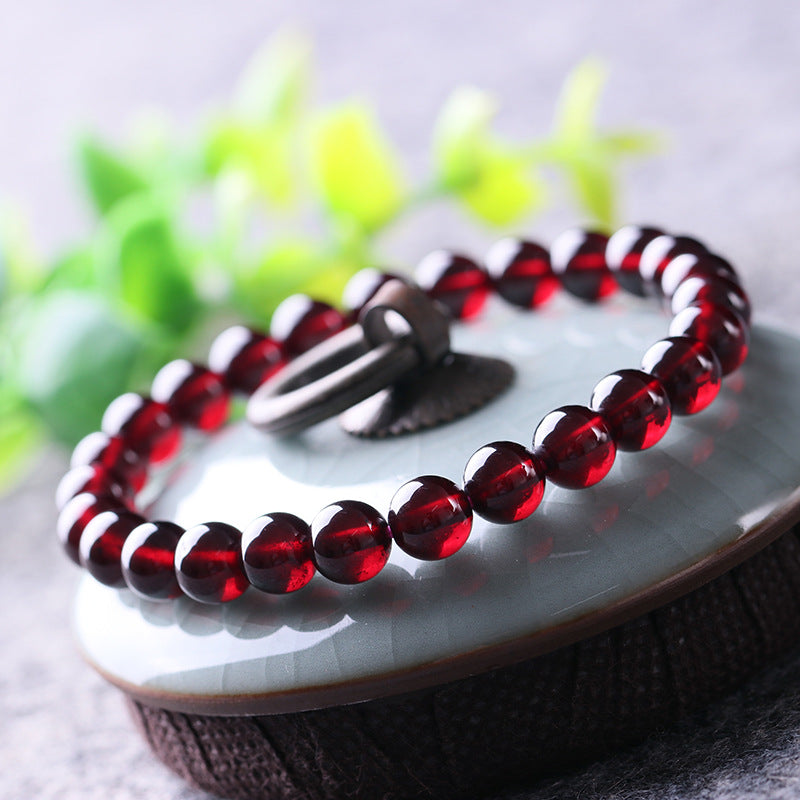 A garnet bead bracelet placed on a light - colored ceramic surface, with deep red, round beads that exhibit a glossy finish.