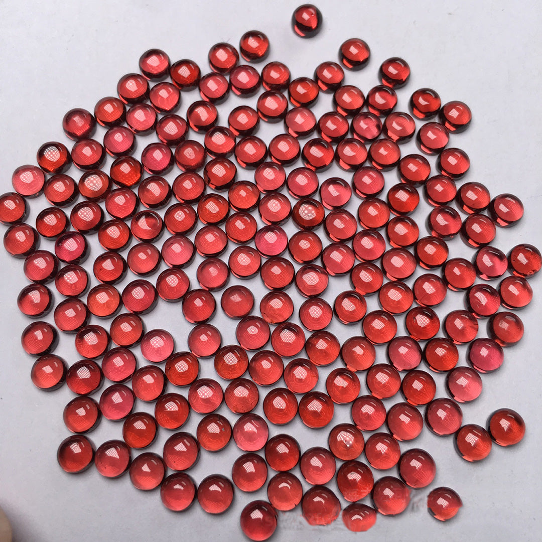 Round red garnets on a white background, many pieces clustered together to create a jewelry texture