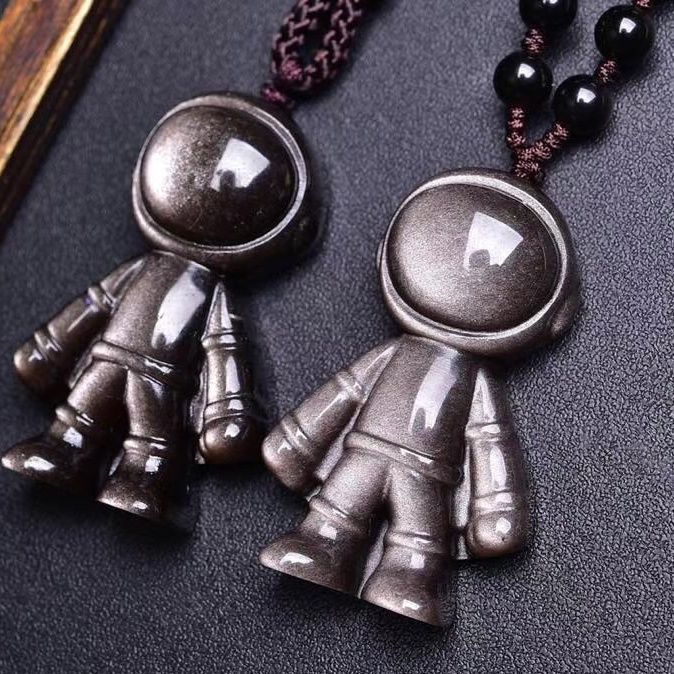 A set of necklaces featuring gold sheen obsidian astronaut - shaped pendants, paired with black obsidian beads, held against a dark background.