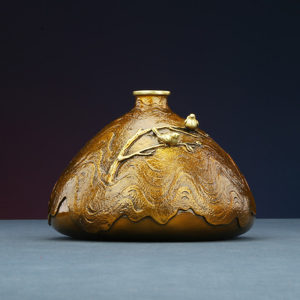 Golden art vase with brass branch and bird decoration against dark gradient background