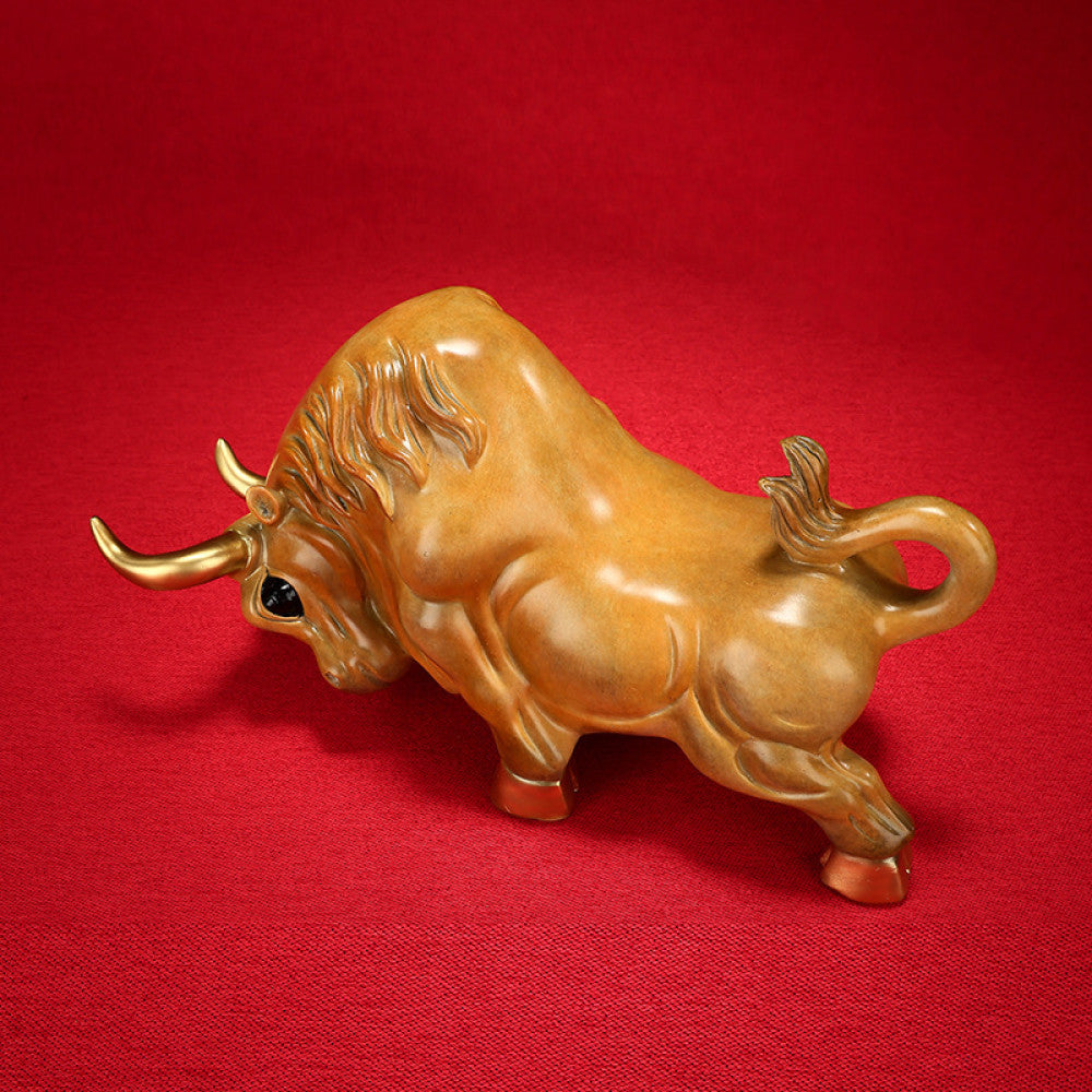 Golden bull statue with detailed craftsmanship, a symbol of strength and good fortune in Feng Shui, displayed as elegant home decor against a red background